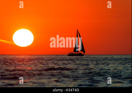 Coucher du soleil est un voilier avec équipage à bord du bateau qui se profile la voile le long de l'océan de l'eau avec un bain de soleil blanc dans le soleil rouge Banque D'Images