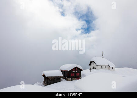 Refuges de montagne couverte de neige et église entourée de nuages bas, Bettmeralp, district de Rarogne, canton du Valais, Suisse Banque D'Images