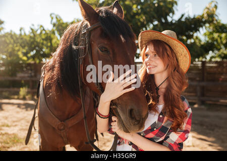 Smiling young woman cowgirl prendre soin et s'étreindre son cheval au ranch Banque D'Images