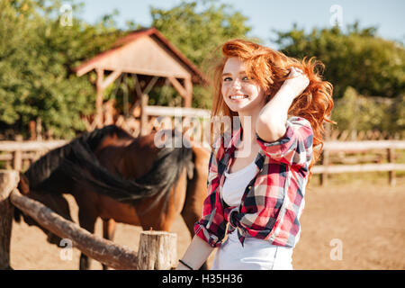 Smiling jolie jeune femme cowgirl avec cheval assis sur ranch Banque D'Images