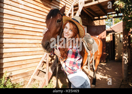 Belle jeune femme souriante en cowgirl hat avec son horse on farm Banque D'Images