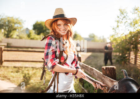 Jeune femme rousse heureux cowgirl la préparation d'une selle à cheval Banque D'Images