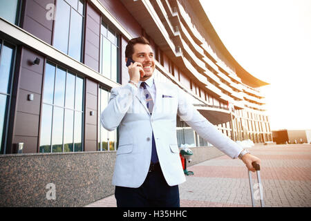 Young happy traveler businessman making appel après son arrivée à l'extérieur de l'hôtel avec ses bagages. Banque D'Images