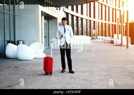 Young happy traveler businessman making appel après son arrivée à l'extérieur de l'hôtel avec ses bagages. Banque D'Images