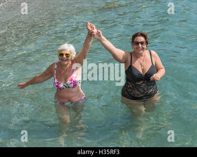 Deux femmes, blonde et brune dodue mature, sont debout dans l'eau clair transparent des galets de mer peu profonde. Banque D'Images