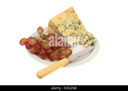 Le fromage Stilton et les raisins avec un couteau à fromage sur une assiette blanche contre isolés Banque D'Images