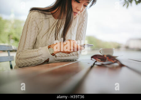 Femme saisissez du texte message sur smart phone dans un café. Image de jeune femme assise à une table à l'aide de téléphone mobile. Banque D'Images