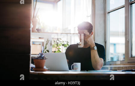 Coup de jeune homme sérieux trouver des idées tout en travaillant sur l'ordinateur portable. Entrepreneur homme assis à son bureau et looking at laptop com Banque D'Images