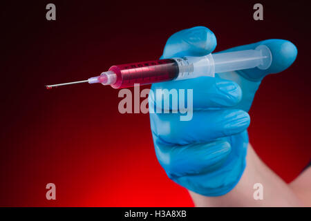 Gant de la main en poussant la seringue sanglante sur fond rouge Banque D'Images