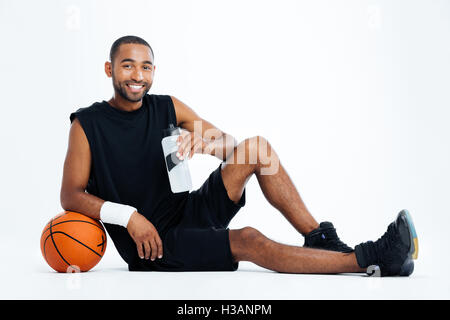 Cheerful young man basket-ball joueur assis et de l'eau potable sur fond blanc Banque D'Images