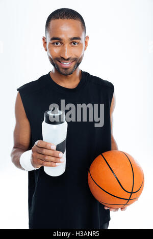 Portrait of a smiling young handsome sportsman holding basket ball et une bouteille d'eau isolé sur fond blanc Banque D'Images