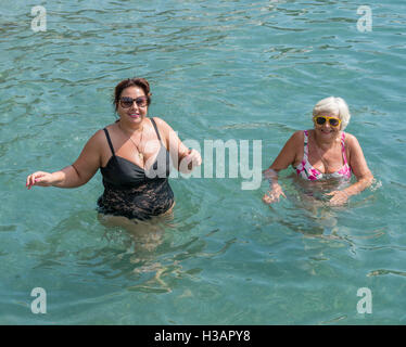 Deux femmes, blonde et brune dodue mature, sont debout dans l'eau clair transparent des galets de mer peu profonde. Banque D'Images