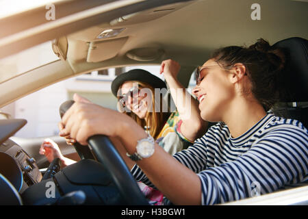 Deux trendy young woman singing le long de la musique comme ils le long d'entraînement dans la voiture à travers la ville vue à travers l'open Banque D'Images