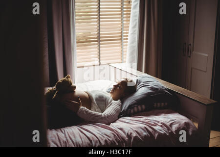 Pregnant woman holding teddy bear sur l'estomac tout en dormant dans la chambre Banque D'Images