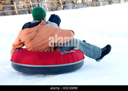 Père avec un jeune fils à cheval sur un snow tube les loisirs d'hiver Banque D'Images