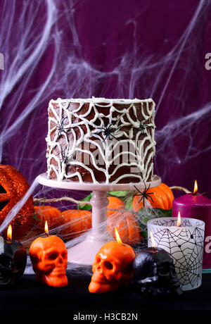 Happy Halloween Party Table avec d'araignée au chocolat Gâteau et brûler des bougies contre purple spider web l'arrière-plan. Banque D'Images