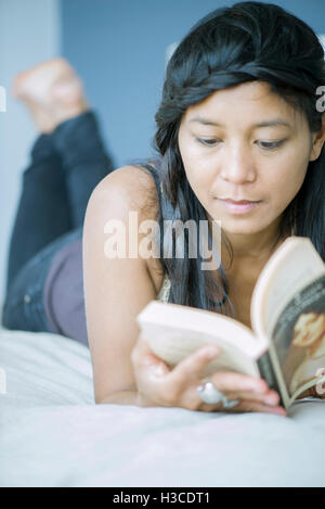 Woman lying on stomach reading book Banque D'Images