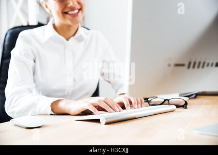 Portrait of a smiling businesswoman de taper au clavier tout en étant assis au bureau 24 Banque D'Images