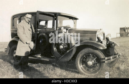 C Antique1930 photographie, l'homme en pardessus pose avec son pied sur la glissière d'une automobile Ford. Emplacement : le Massachusetts, New England, USA. SOURCE : tirage photographique original. Banque D'Images