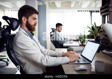 Vue latérale du businessman using laptop in creative office Banque D'Images