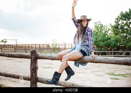 Cheerful attractive young woman girl sitting on fence et s'amuser Banque D'Images