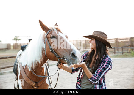 Cheerful attractive young woman cowgirl jouant à cheval en campagne Banque D'Images