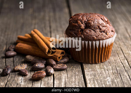 Le muffin au chocolat savoureux et les fèves de cacao sur la vieille table en bois. Banque D'Images