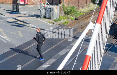 Homme qui court à travers les lignes de chemin de fer au passage à niveau que les portes sont descendus. Banque D'Images