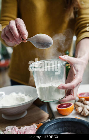 Une femme le mélange des ingrédients dans une casserole, le sucre, les oranges, les pétales et le gingembre. Banque D'Images