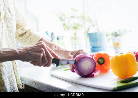 Une femme debout dans une cuisine, la coupe d'un oignon rouge et poivrons sur une planche à découper. Banque D'Images