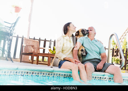 Un couple assis sur le bord d'une piscine, avec leurs chiens. Banque D'Images