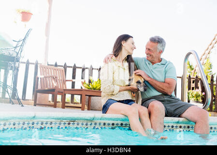 Un couple assis sur le bord d'une piscine, avec leur chien entre eux. Banque D'Images