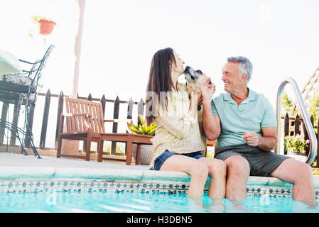 Un couple assis sur le bord d'une piscine, avec leur chien. Banque D'Images