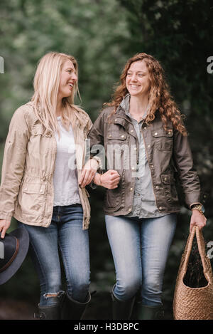 Deux femmes dans les bras de marcher dans des manteaux et des bottes le long d'un chemin de pays avec un panier. Banque D'Images