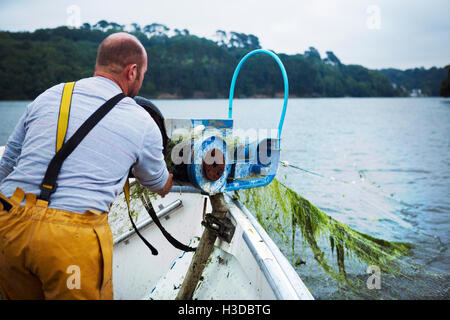 Un pêcheur en jaune les limicoles sur son bateau dans le bobinage de filet de pêche de l'eau. Banque D'Images