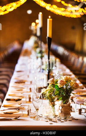 Une salle de mariage décoré pour une partie, avec fairy lights et une longue table set pour le dîner. Banque D'Images