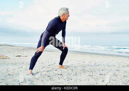 Senior man wearing wetsuit standing sur une plage de sable. Banque D'Images