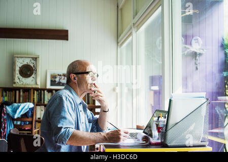 Un homme assis à un bureau à la maison, travailler sur un ordinateur portable. Banque D'Images