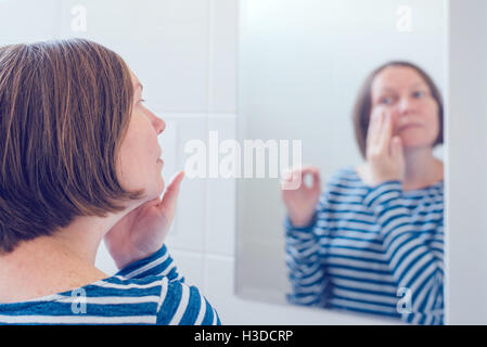 Jeune femme adulte, l'application de crème anti-vieillissement devant le miroir, selective focus Banque D'Images