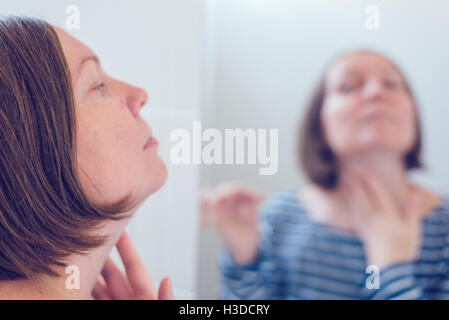 Jeune femme adulte, l'application de crème anti-vieillissement devant le miroir, selective focus Banque D'Images