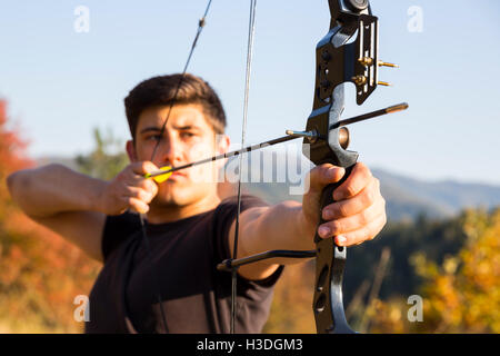 Un archer arc à son dessin dans un champ dans la forêt au début de l'automne. Les arbres d'automne en arrière-plan. Banque D'Images