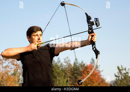 Un archer arc à son dessin dans un champ dans la forêt au début de l'automne. Les arbres d'automne en arrière-plan. Banque D'Images