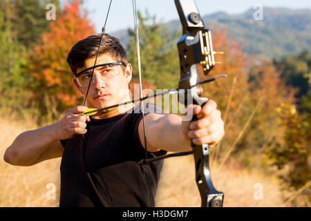 Un archer arc à son dessin dans un champ dans la forêt au début de l'automne. Les arbres d'automne en arrière-plan. Banque D'Images