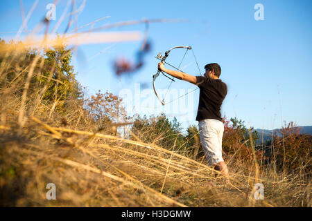 Un archer arc à son dessin dans un champ dans la forêt au début de l'automne. Les arbres d'automne en arrière-plan. Banque D'Images