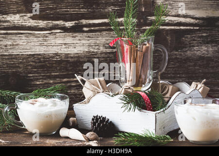 De Lait de poule avec la crème fouettée en verre sur table rustique en bois, vacances de Noël la décoration de table et traiter Banque D'Images