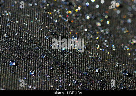 Gouttes d'eau sur un matériau imprégné de noir à la lumière du soleil. Banque D'Images