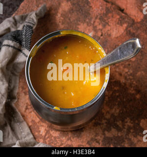 Boite de conserve de soupe de carottes avec cuillère, debout sur une serviette de cuisine et de l'argile sur vieux fer rouillé. Style rustique foncé. Banque D'Images