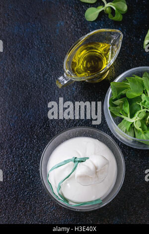 Ensemble de fromage italien lié à la saumure de burrata servis avec salade de maïs frais et d'huile d'olive en plus de coupes en verre textures sombres backgrou Banque D'Images