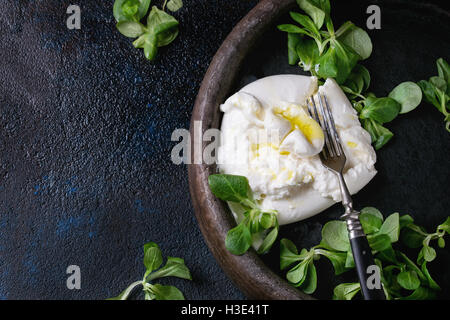 Tranches de fromage italien burrata avec fourche vintage, frais salade de maïs et l'huile d'olive dans le bac d'argile sombre sur fond de texture. Plus de Banque D'Images