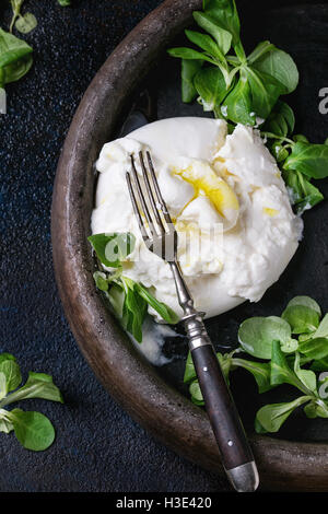 Tranches de fromage italien burrata avec fourche vintage, frais salade de maïs et l'huile d'olive dans le bac d'argile sombre sur fond de texture. Plus de Banque D'Images